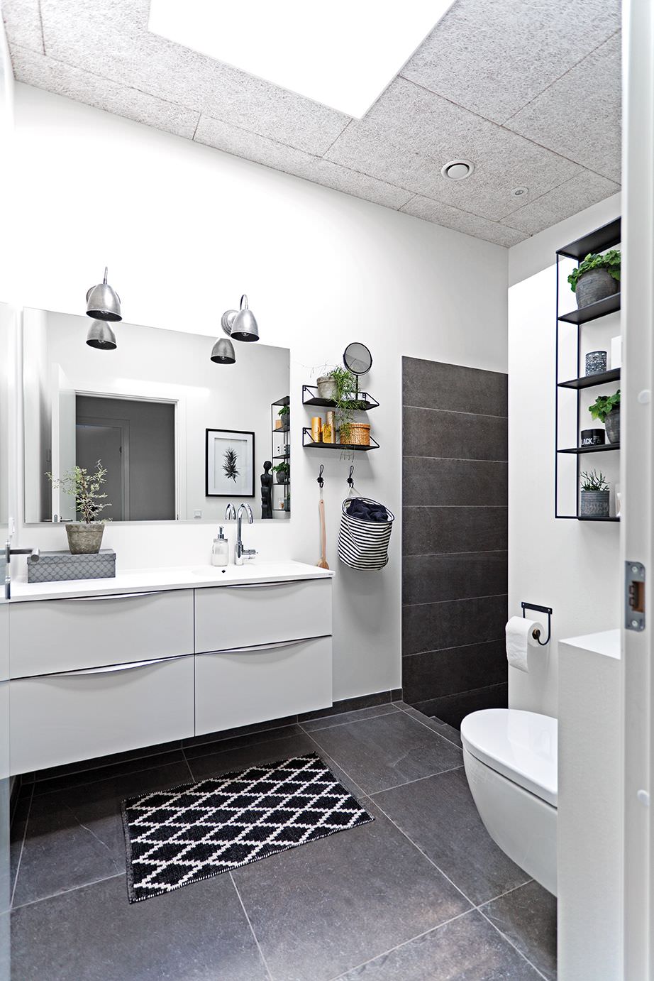 دکوراسیون سرویس بهداشتی و حمام مدرن و شیک با دیوار، روشویی و توالت فرنگی سفید که رنگ ثانویه و سرامیک کف سیاه رنگ دارد